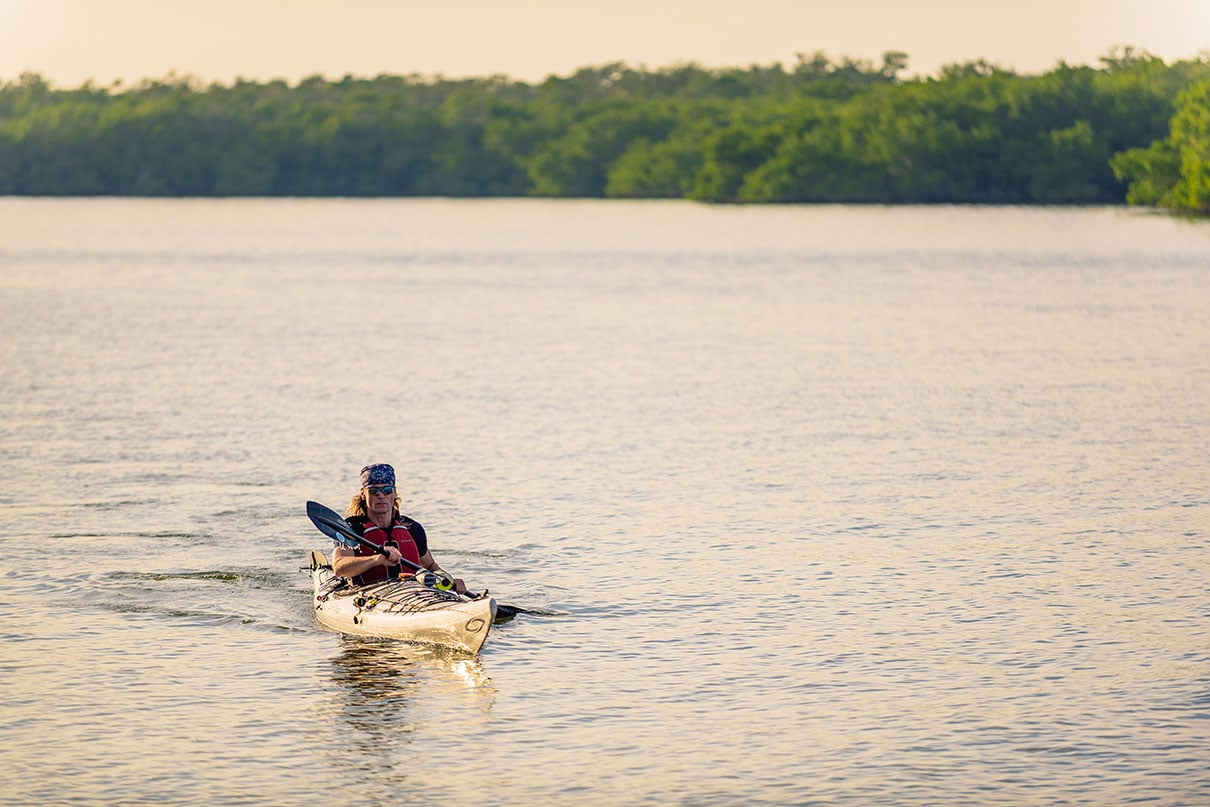 man with bandana paddles a sea kayak across water in Florida