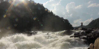 a person films from the rocky shore while another person goes whitewater kayaking in India