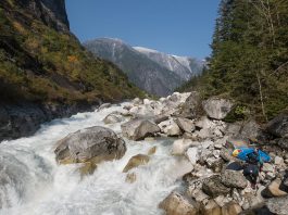 Person carrying whitewater kayak around river full of boulders