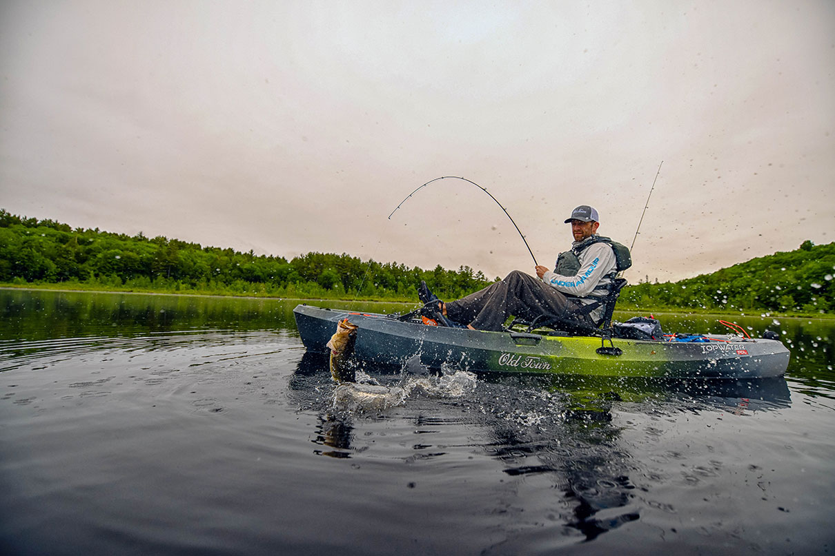 man reals in bass caught from a sit-on-top fishing kayak