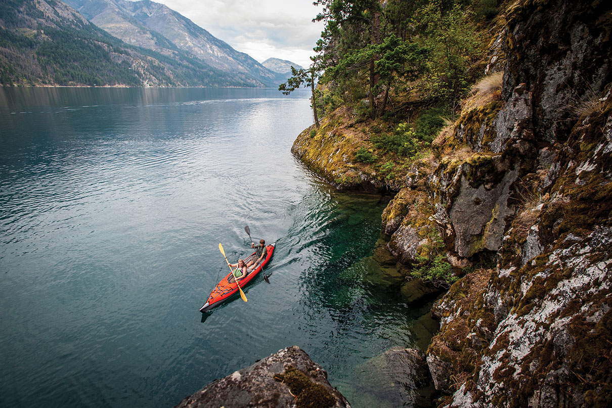 two people paddle through a picturesque mountainous landscape in a tandem inflatable kayak