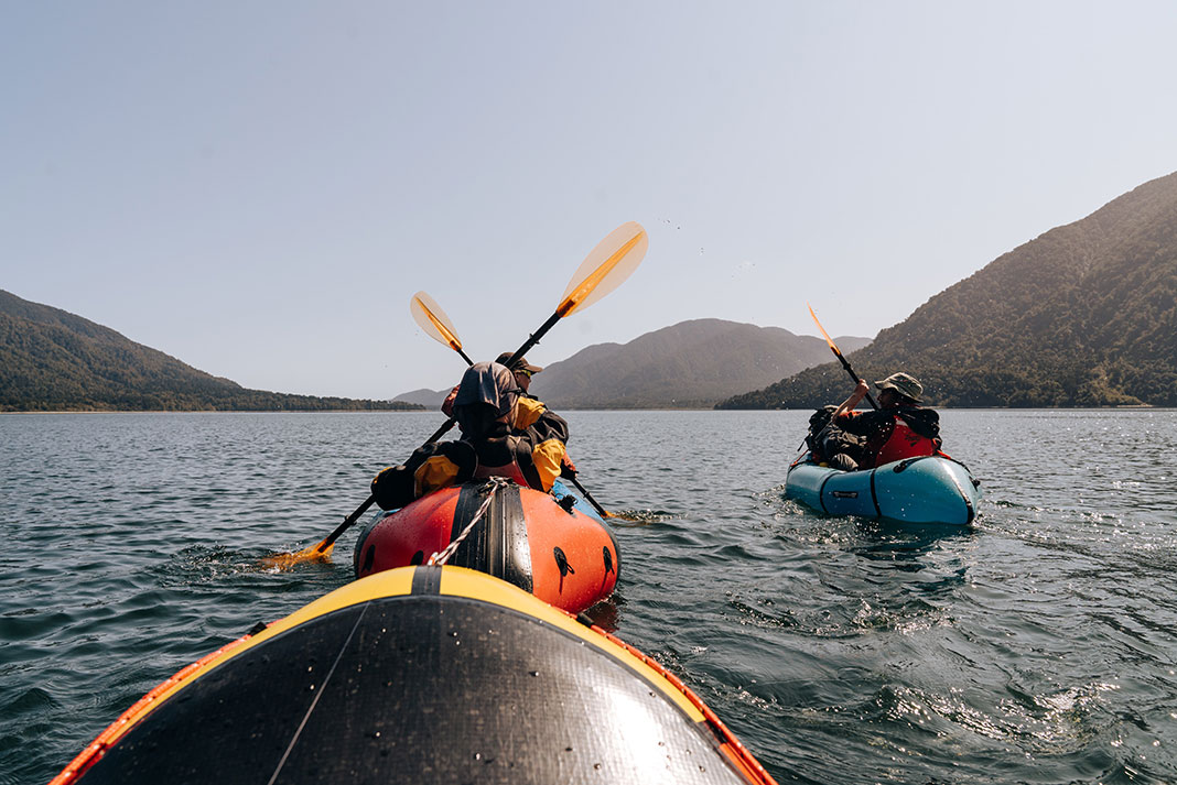 people packraft on expansive waters surrounded by hills
