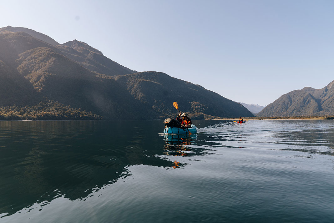 people packraft on expansive waters surrounded by hills
