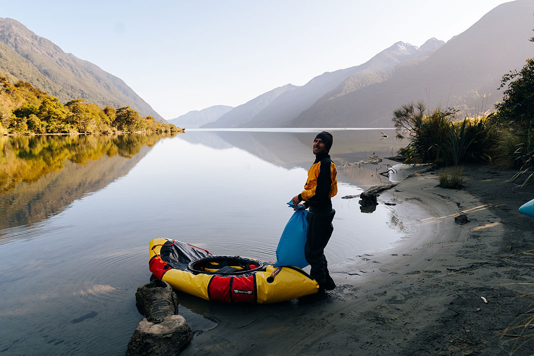 man stands beside his packraft, inflating it and loading it for the day's paddle