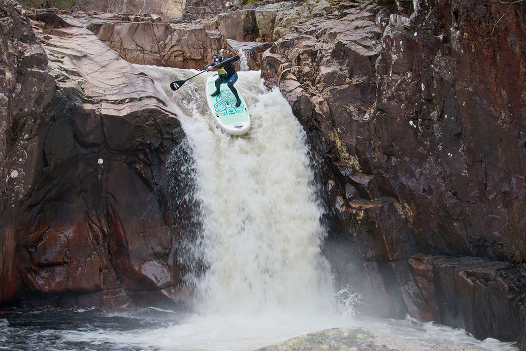 man paddleboards over Right Angle Falls in the Scottish Highlands