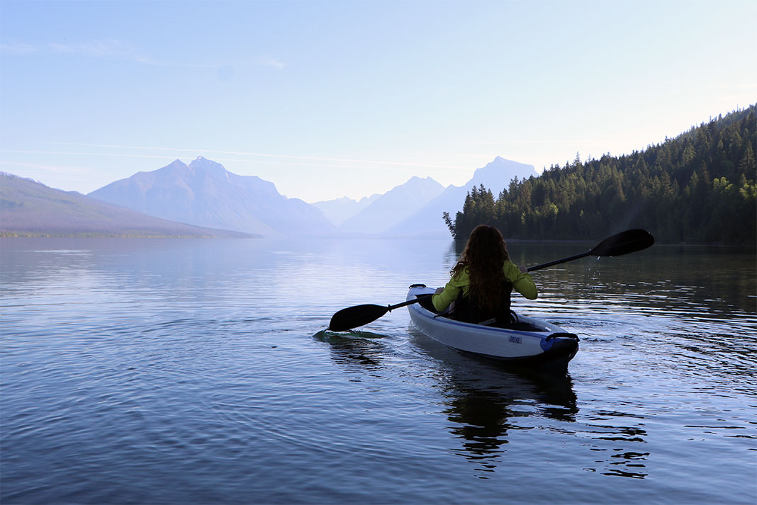 woman paddles an inflatable kayak on a peaceful lake with mountain backdrop