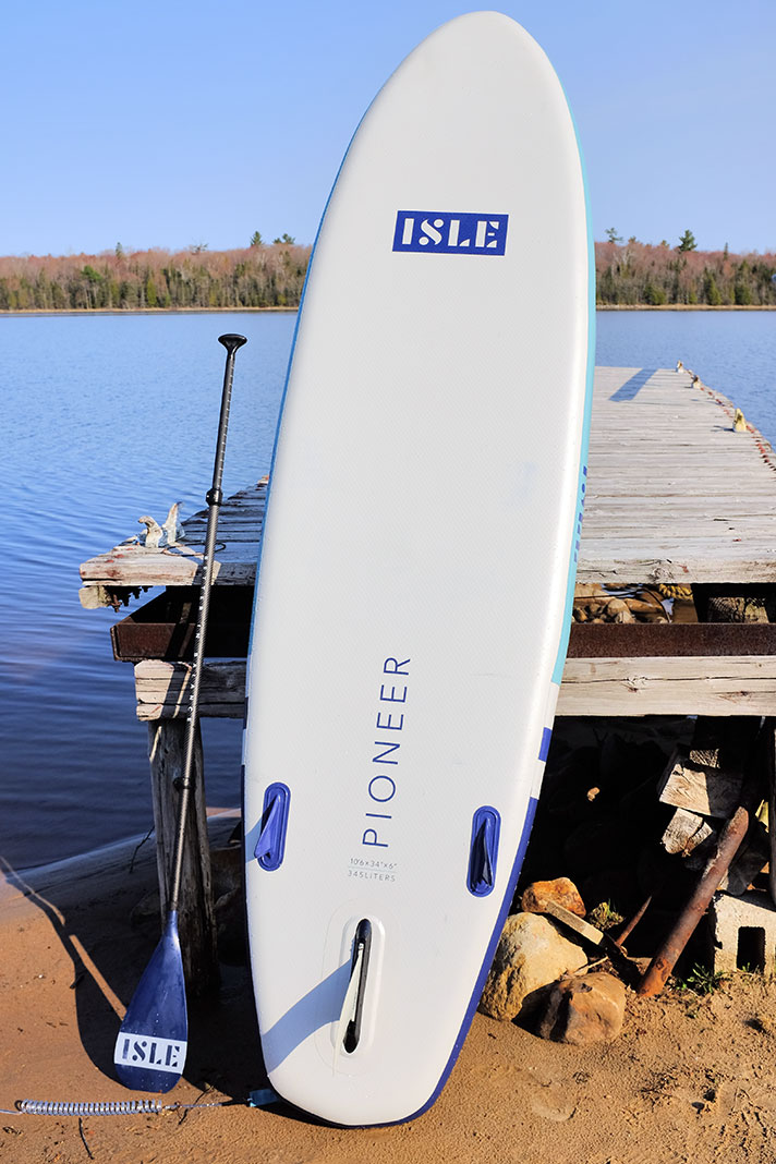 the ISLE Pioneer 2.0 paddleboard stands up propped on a dock
