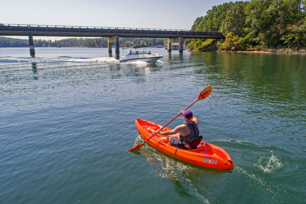 man paddling the Perception Tribe 9.5 near a bridge and passing power boat