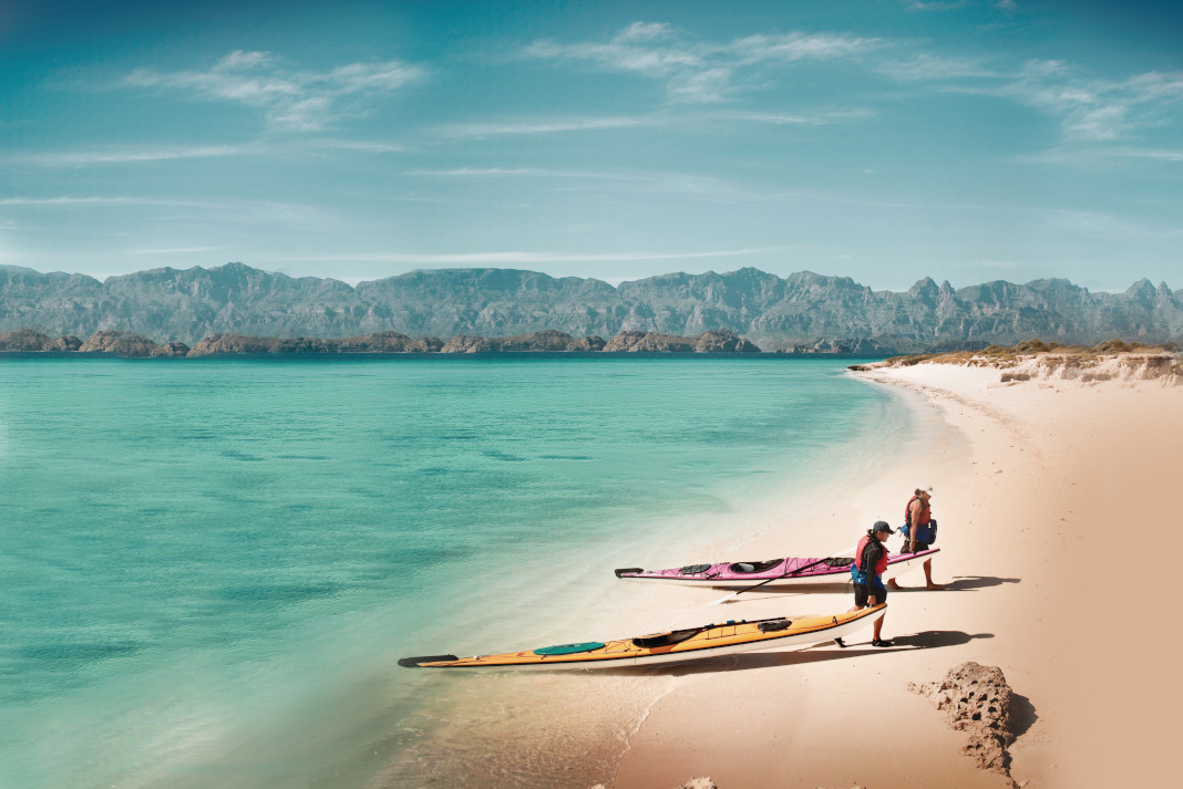 Two people carrying kayaks up beach in Baja Sur.