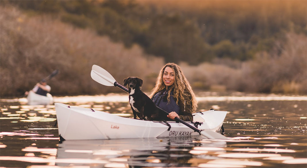 woman paddles an Oru Kayak with dog