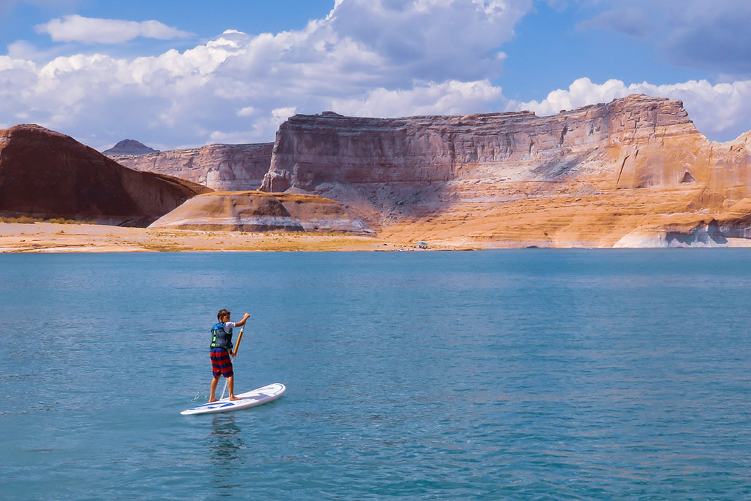 a young man paddles a paddleboard in front of desert mesas