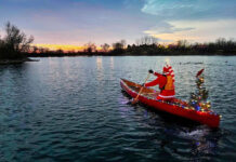 person in santa suit paddles a canoe decorated with Christmas lights