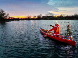 person in santa suit paddles a canoe decorated with Christmas lights