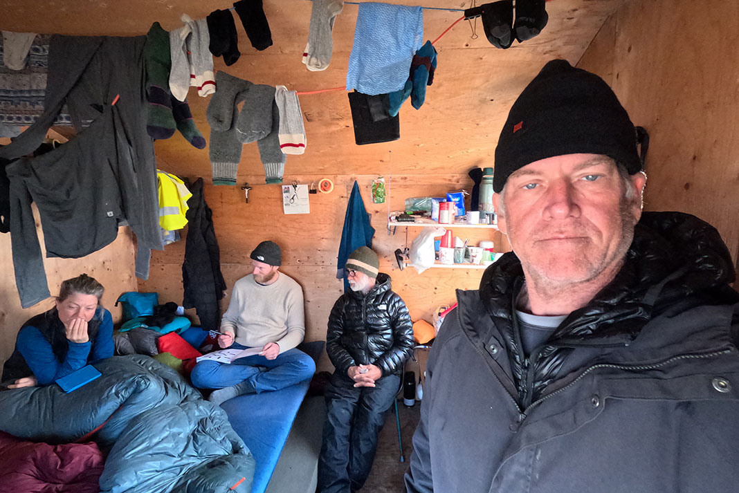 paddlers pose in an Arctic shack with laundry hanging all around