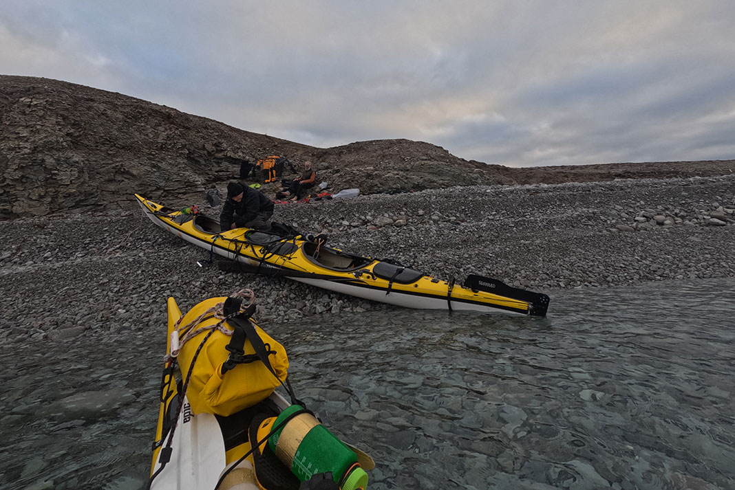 Arctic kayakers pull their boats onto a pebbly shore