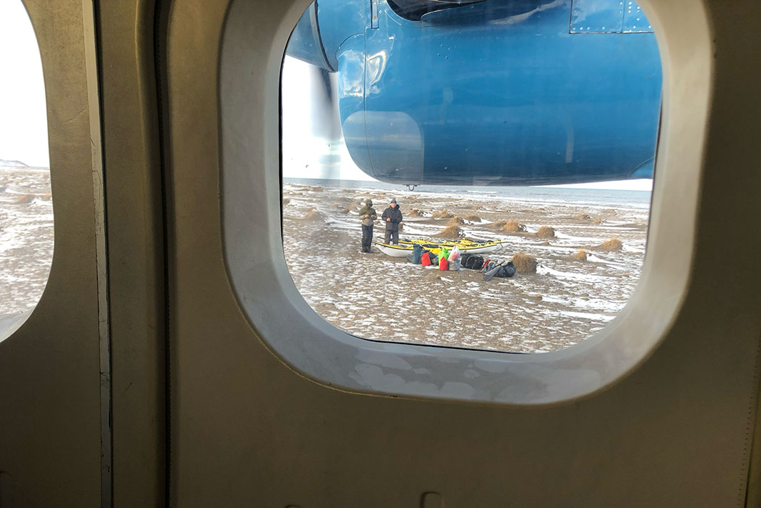 view out of a small airplane window at paddlers standing with bags on the Arctic tundra