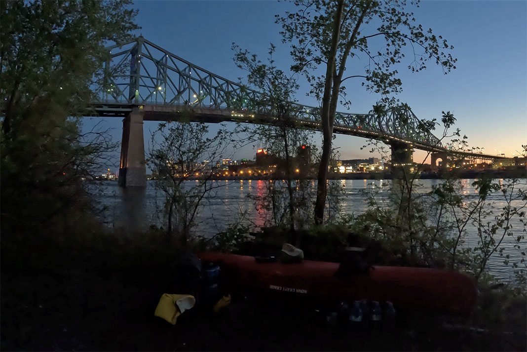 canoe on shore at dusk near a large bridge in Montreal