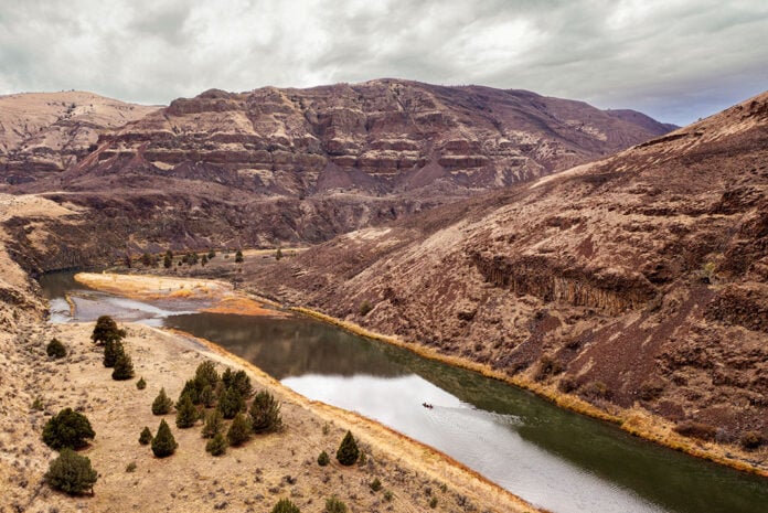 canoeist with permit travels down the John Day River surrounded by massive striated rock cliffs