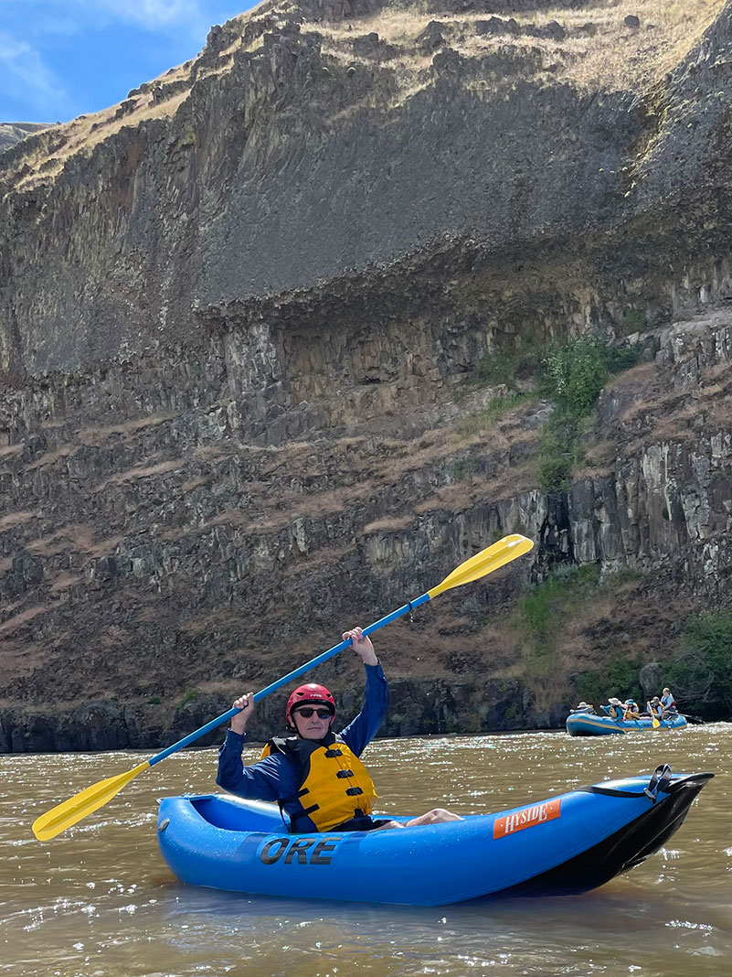 older man holds his kayak paddle aloft while paddling the John Day River