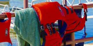 two Stohlquist life jackets hang over a fence with a towel