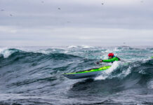 man paddles a Current Designs sea kayak in surf