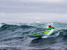 man paddles a Current Designs sea kayak in surf