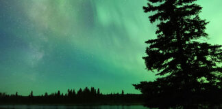an overturned canoe sits on the bank at a campsite under a vivid night sky with northern lights