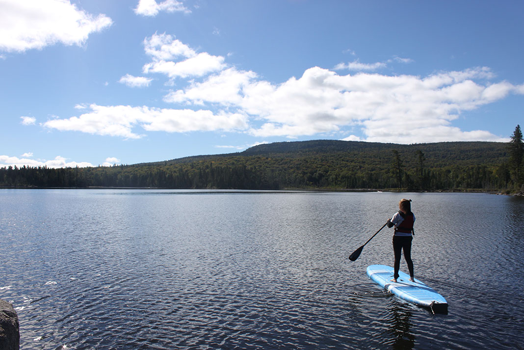 woman looks out over a Quebec lake from her paddleboard