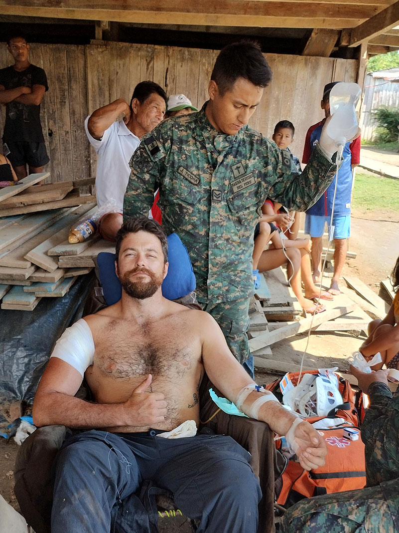 wounded man gives thumbs up while being attended by army medic after a gunfight during his Amazon River expedition