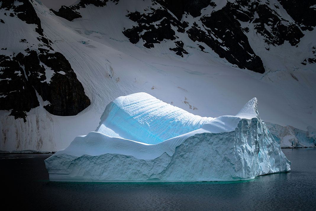 dramatic iceberg in front of rocky cliff in Antarctica