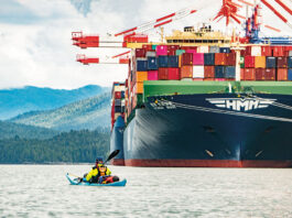 man paddles a kayak in front of a large container ship in British Columbia
