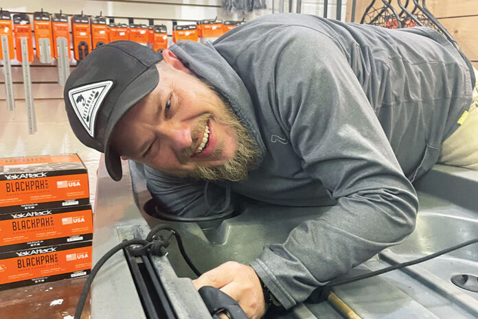 man leans over a fishing kayak while doing custom outfitting at a kayak fishing retailer