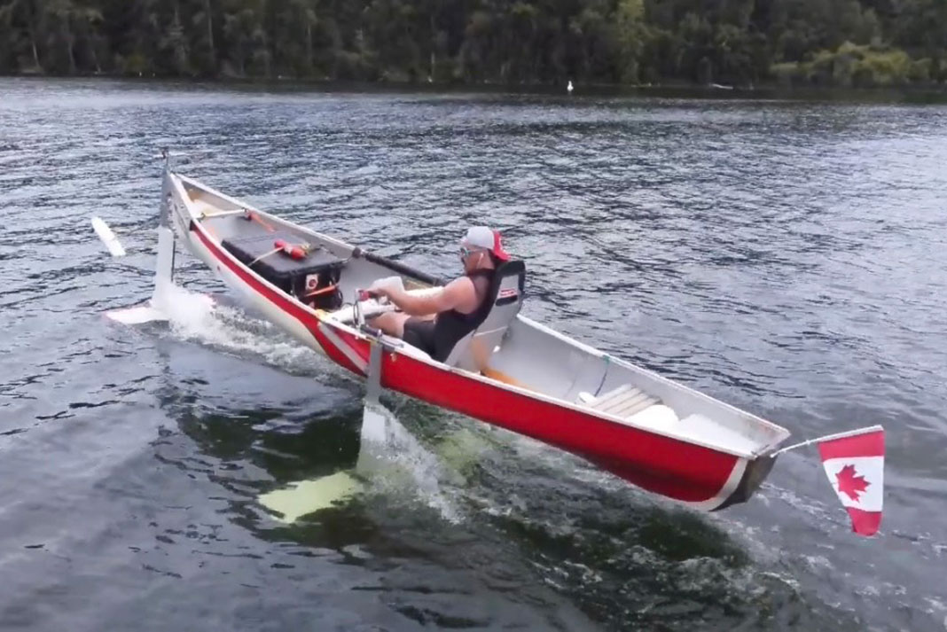 man travels on a lake in a hydrofoil canoe with a Canadian flag on the back