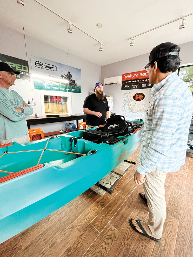 three men stand in a kayak fishing shop around a kayak customization project