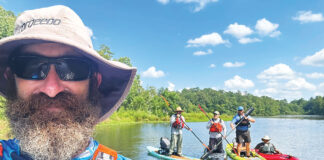 man in bucket hat and PFD takes photo with three kayak anglers posing on boats in the background
