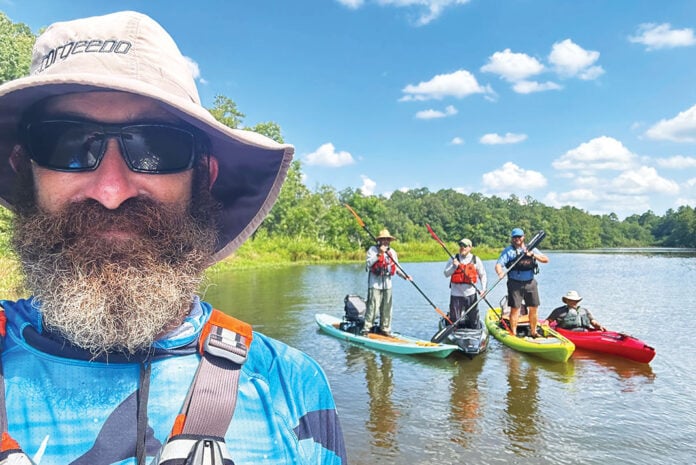 man in bucket hat and PFD takes photo with three kayak anglers posing on boats in the background