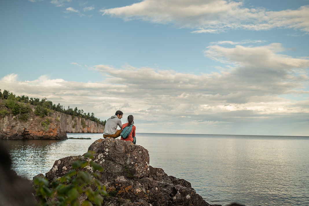 two people sit on a rocky point overlooking Lake Superior