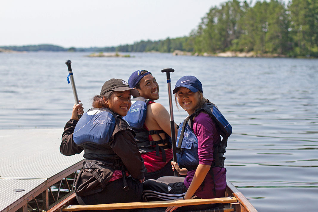 three young people pose in a canoe before taking off to paddle