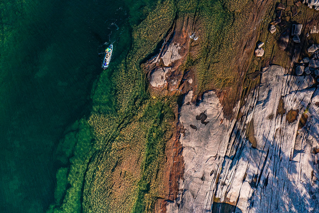 overhead photo of a person paddling an electric sup through blue water past a rocky shelf