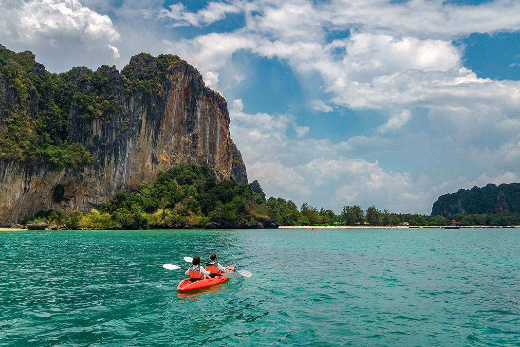 people paddle among towering rock pillars in Thailand