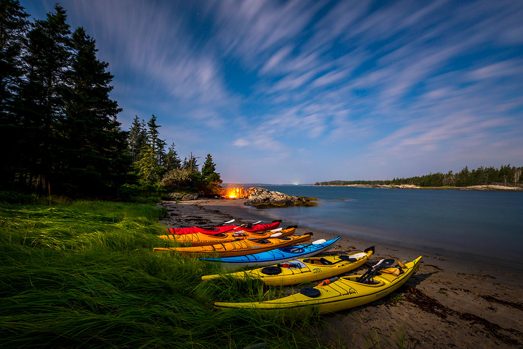 a group of kayaks are lined up along a shore at a campsite at dusk
