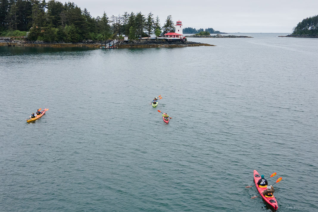 a group of kayakers paddle toward a lighthouse in Alaska