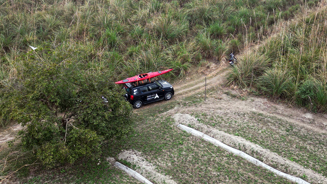 a jeep with touring kayak on roof drives past tropical paddocks