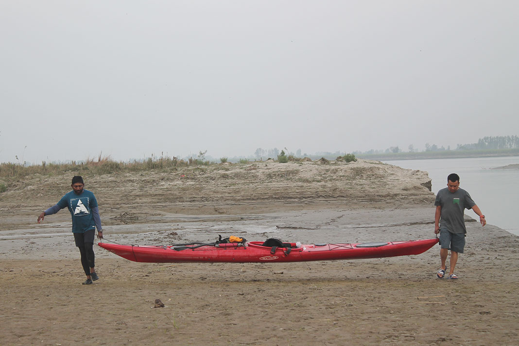 two people carry a red sea kayak along a sandy riverbank