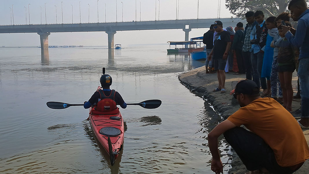 Rency Thomas launches his kayak onto the Ganges River while a group of men watch