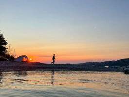 a woman walks around her waterside campsite at dusk while on a microadventure