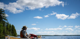 an older man sits in an ultralight canoe and looks out across a northern lake