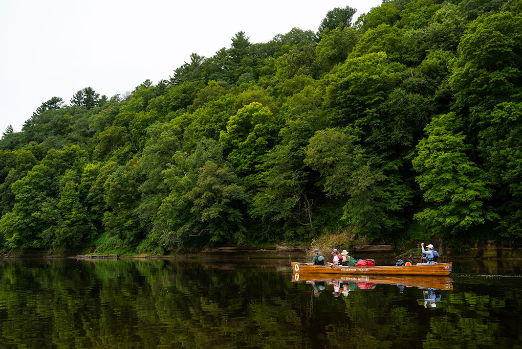 a family paddles their canoe along the forested shoreline of the St. Croix River