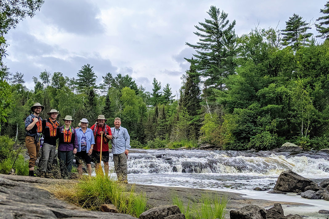 a group of canoeists pose in front of a waterfall
