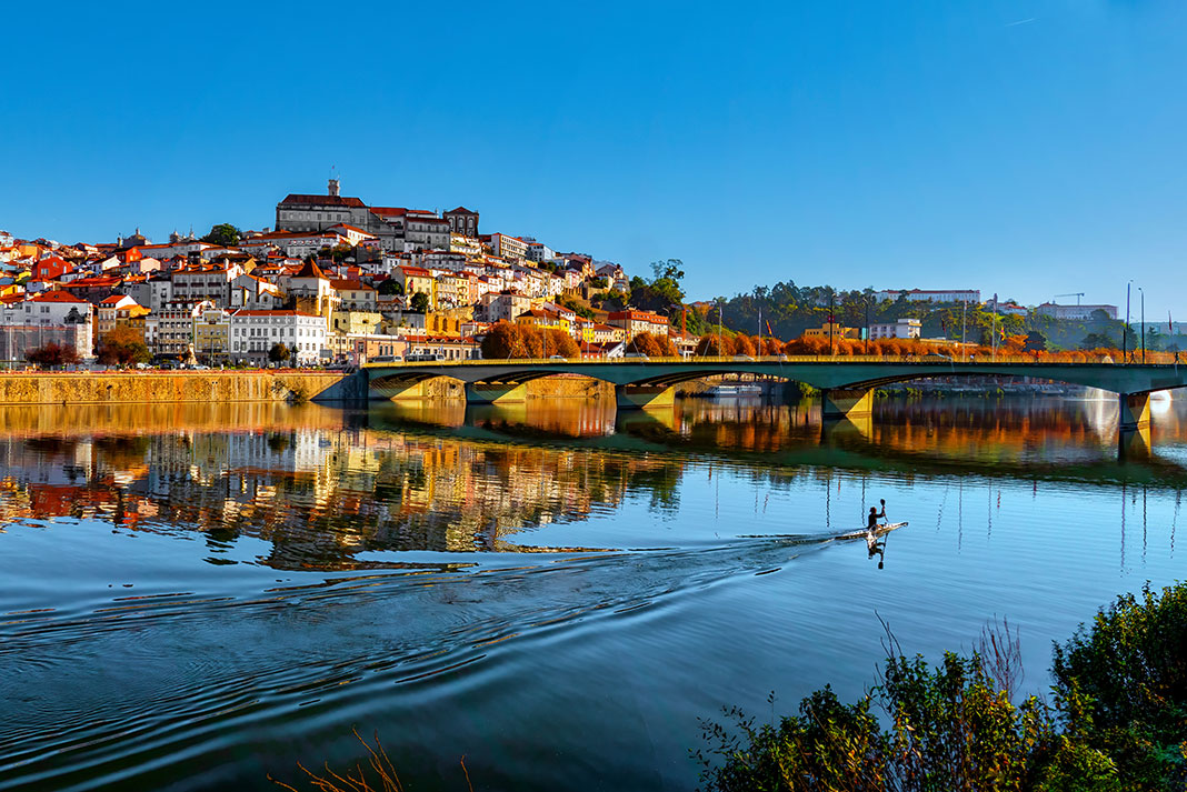 a kayaker paddles toward a bridge near a picturesque city in Portugal